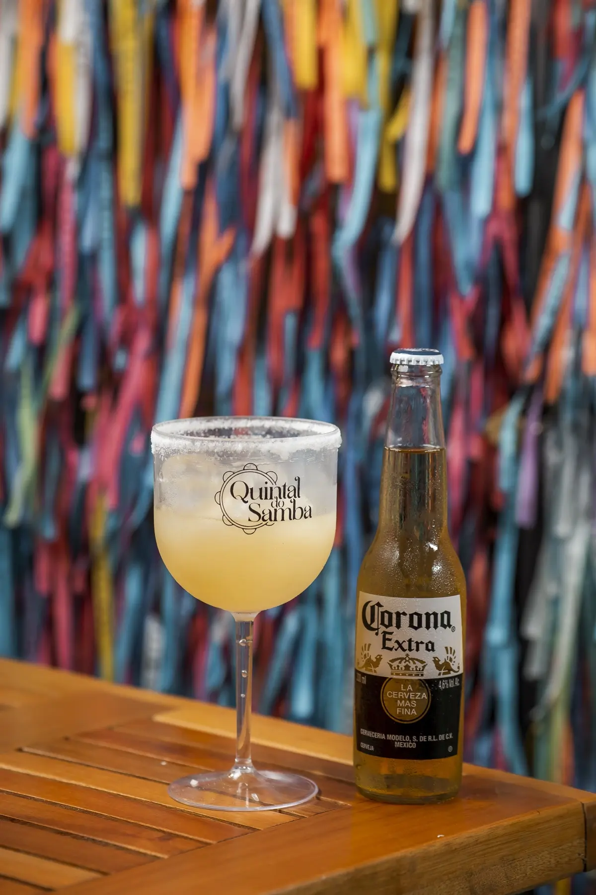 Taça com a marca do Quintal do Samba e garrafa sobre mesa de madeira